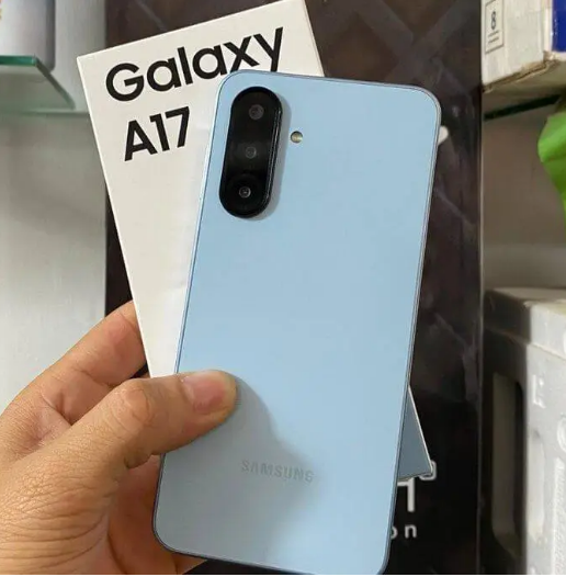 Mão sênior segurando o smartphone Samsung Galaxy A17 na cor azul clara, mostrando a parte traseira e as câmeras do aparelho, ideal como celular para idoso.