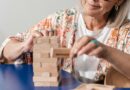 Idosa sorridente montando um quebra-cabeça colorido em uma mesa de madeira, representando os estímulos cognitivos e a prevenção do Alzheimer .