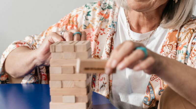 Idosa sorridente montando um quebra-cabeça colorido em uma mesa de madeira, representando os estímulos cognitivos e a prevenção do Alzheimer .