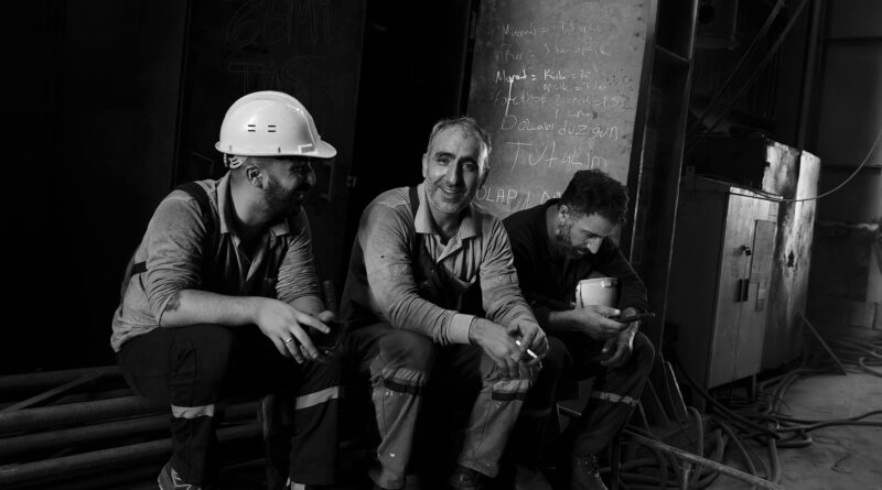 Fotografia antiga em tons de preto e branco mostrando operários brasileiros de fábrica reunidos durante o intervalo de trabalho.