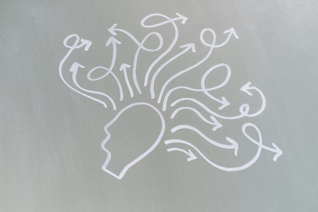 Desenho em linhas brancas de uma cabeça humana com setas saindo da mente sobre um fundo cinza, representando os estímulos cognitivos e a prevenção do Alzheimer .