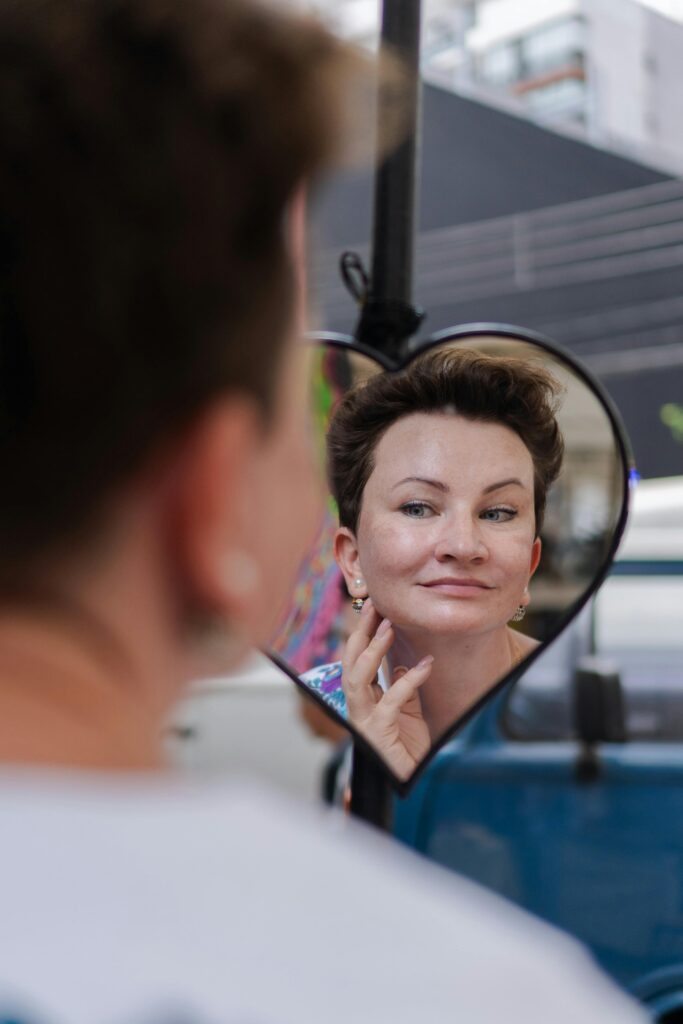 Mulher sorridente olhando o reflexo do seu rosto em um espelho de mão em formato de coração, cuidando da beleza na terceira idade.
