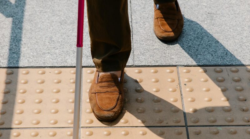 Homem idoso caminhando com apoio de bengala por uma calçada urbana, simbolizando as dificuldades de acessibilidade nas cidades brasileiras.