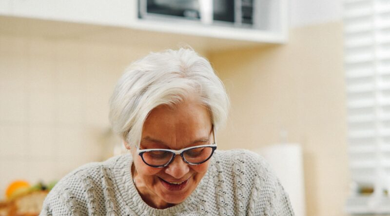 Mulher idosa sorridente e tranquila anotando datas importantes em um calendário de mesa de papel, sentada na sala de sua casa bem iluminada.