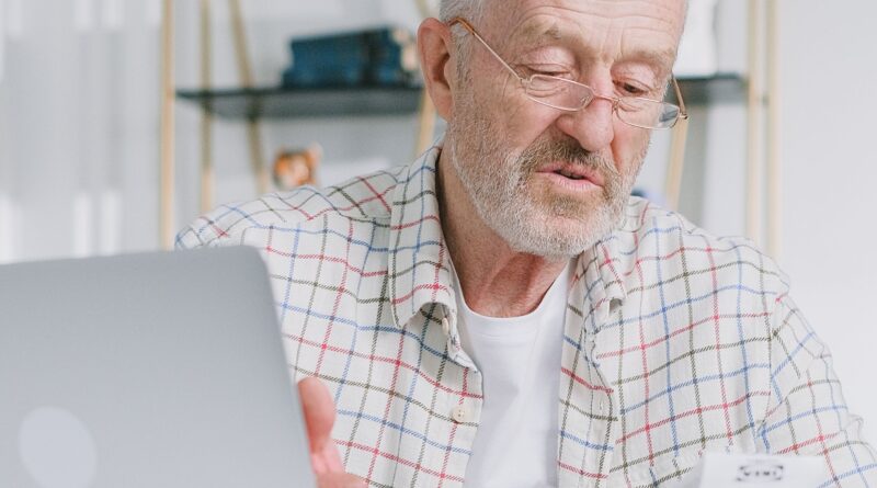 Homem idoso de óculos olhando confuso para a tela de um computador portátil na mesa de casa, analisando o extrato do seu benefício previdenciário.